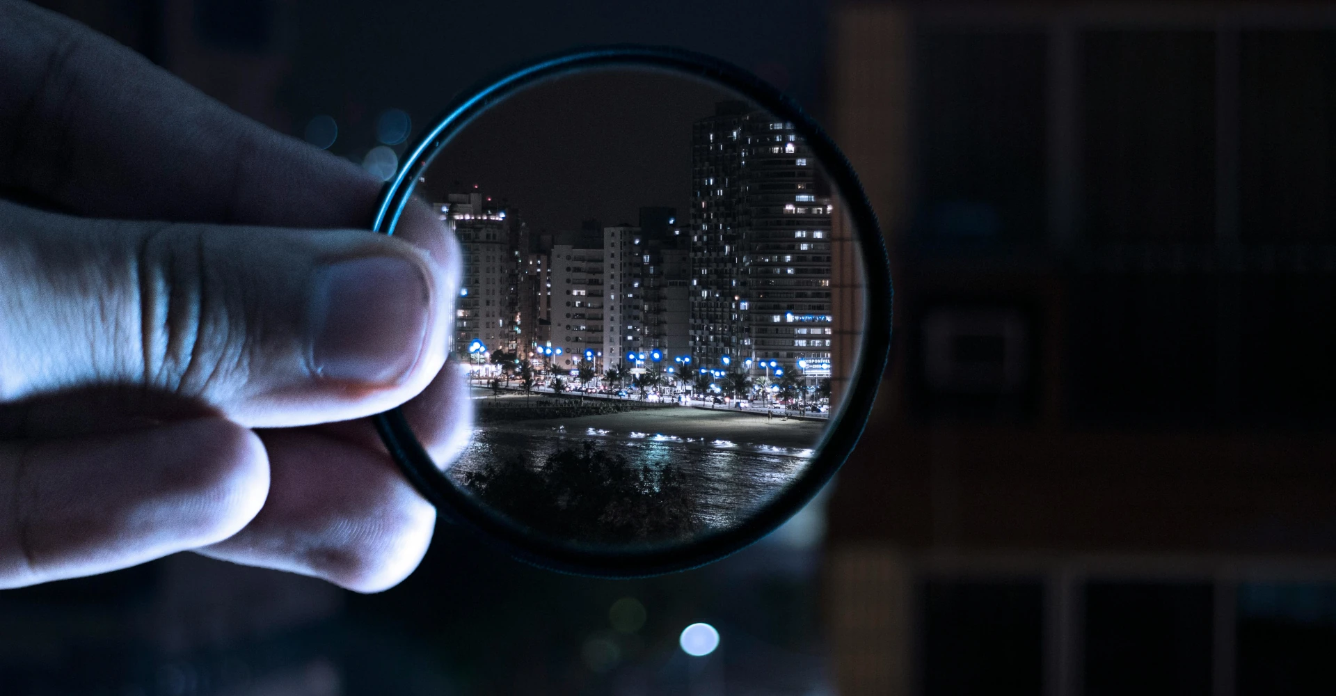 Hand holding a magnifying glass to a night time citscape